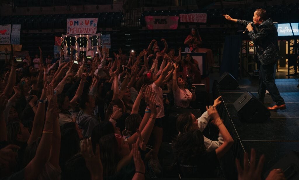 Comedy hypnotist Richard Barker on stage engaging entire audience with hands raised during interactive comedy hypnosis show